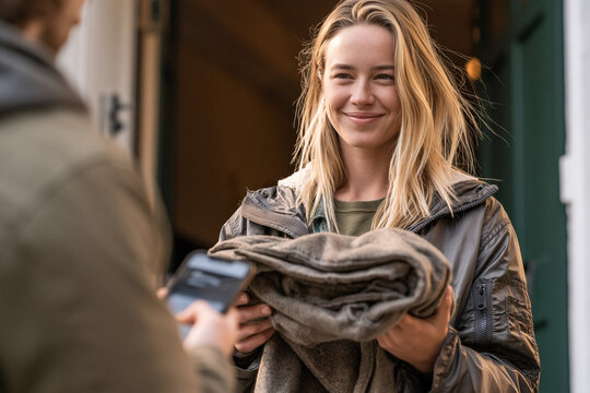 Young woman handing over secondhand coat to buyer at apartment door