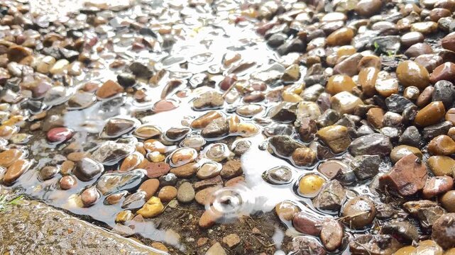 Detailed close-up of heavy rain splashing onto puddle of water with pebbles in nature outdoor landscape.