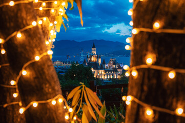 Illuminated castle-inspired of Vinpearl in VinWonders theme park overlook a scenic bay at dusk, creating a magical waterfront cityscape with mountains, dramatic clouds, and evening lights. © olinchuk