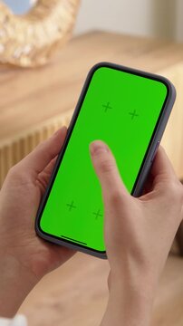 Woman sit use digital tech cell phone with green screen mock up. Hand scroll phone web site, swipe like photos. Girl hold mobile closeup. Chroma key page. Cozy home background. Online app copy space.