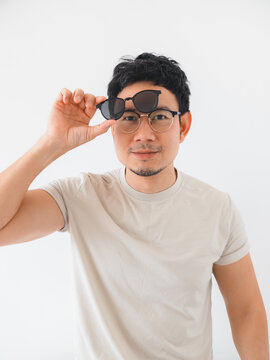 Young Asian man wearing eyeglasses, holding sunglasses above his forehead on a white background.