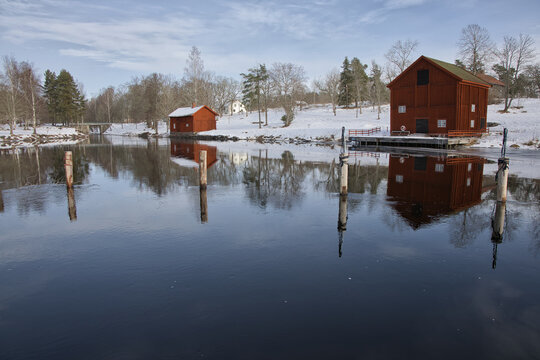A classic red Swedish wooden house by the water, reflected in Borgvik. Winter scene with snow and traditional Falun red architecture in Vrmland, Sweden.