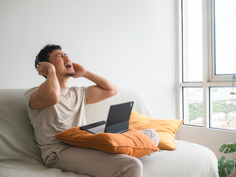 Young man feeling overwhelmed by noise, covering ears with headphones while working from home.