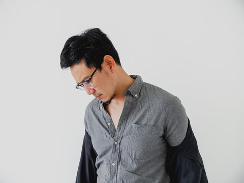 Thoughtful Asian man in glasses looking down with a focused expression.