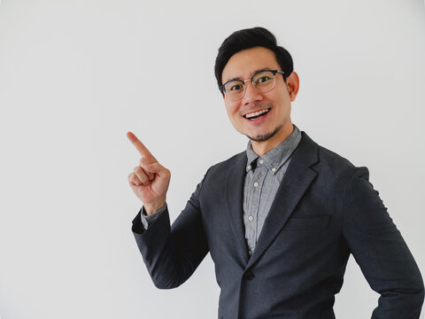 Happy young Asian man in suit jacket pointing finger upwards, presenting information on white background.