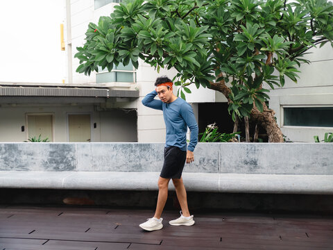 Fit young Asian man in sportswear walking on a wooden deck in an urban setting.