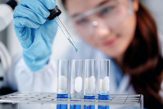 Scientific researcher conducting laboratory experiment transferring blue liquid to test tubes for medical chemical analysis in science lab