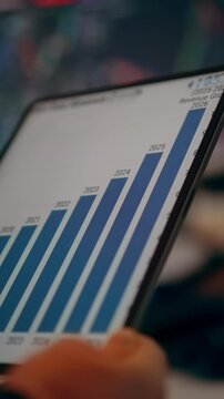 Growing bar chart financial stats revenue projections tablet screen. Close up view displaying a rising blue bar graph with year labels representing corporate growth and success. In the background blur