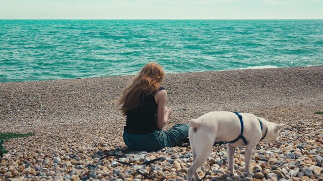 Red Haired Woman Walking White Dog Along Pebble Beach by the Ocean