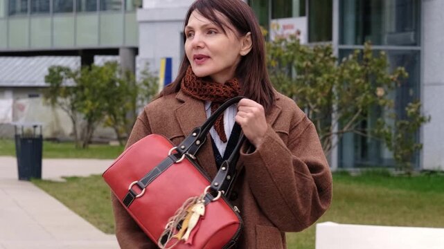 A natural lifestyle portrait shows a woman pausing outside a modern building, looking aside with a slight smile and composed posture. The footage evokes autumn calm, independence, style, and