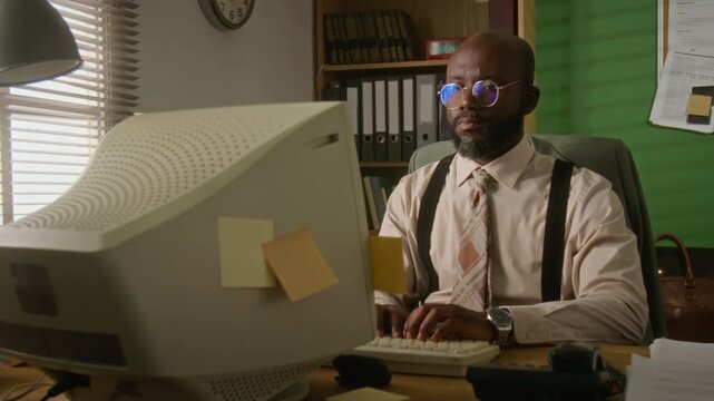 African American man typing on vintage CRT computer in retro office. Footage is perfect for historical technology documentaries or retro business marketing campaigns