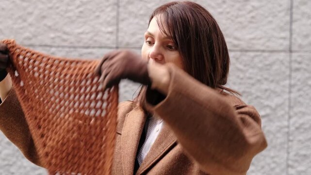 The camera frames a woman over fifty adjusting a knitted hat and leather gloves, with relaxed eyes and warm expression. This scene fits graceful aging, personal style, autumn wardrobe, and confidence.