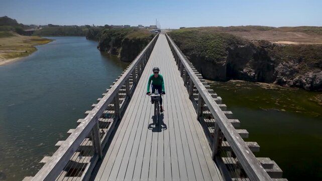 A woman enjoys biking across Pudding Creek Bridge in Fort Bragg California near Mendocino out for adventure.