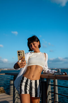 Female blogger shoots content for social networks. Smiling tourist takes a selfie on her mobile phone against the backdrop of the sea.