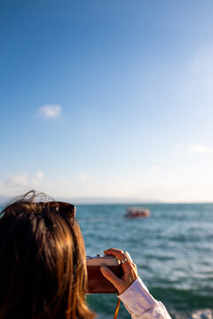 girl taking picture of ship standing on embankment. Beautiful female tourist enjoying sea view while relaxing on weekend. girl using camera.
