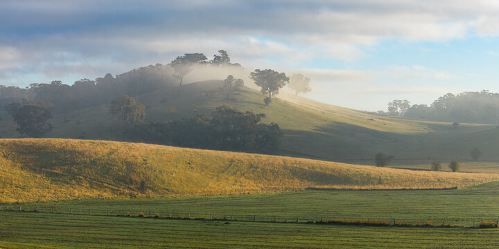 Morning fog and sunshine over hills on green farmland