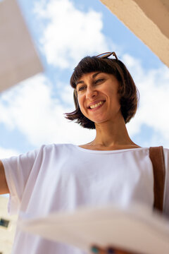 woman reading received letter standing among mailboxes. Portrait of smiling young woman opening mailbox studying received mail.