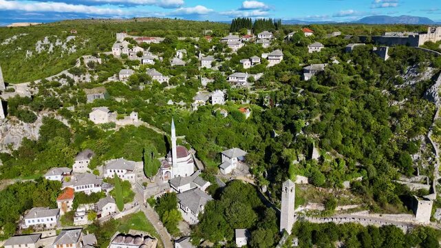 Aerial view of the historic village of Pocitelj with stone houses, mosque, and fortress ruins on a green hillside in Pocitelj, Federation of Bosnia, Bosnia and Herzegovina.