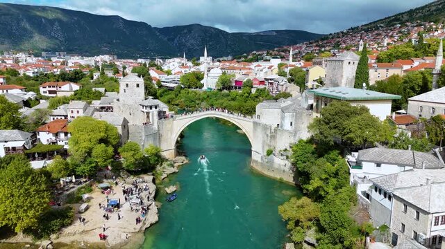 Aerial view of the historic Old Bridge Mostar spanning the turquoise Neretva River with surrounding stone buildings and lush greenery in Mostar, Federacija Bosne i Hercegovine, Bosnia and Herzegovina.