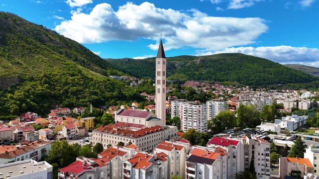 Aerial view of the Franciscan Church of St. Peter and Paul with its bell tower, surrounded by residential buildings and green hills in Mostar, Federation of Bosnia, Bosnia and Herzegovina.