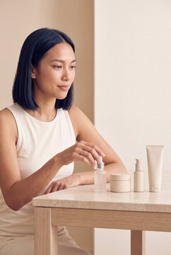 Woman applying serum from dropper with cosmetic jars and tube on table for skincare routine and beauty product display background image for cosmetic banner and ecommerce layout