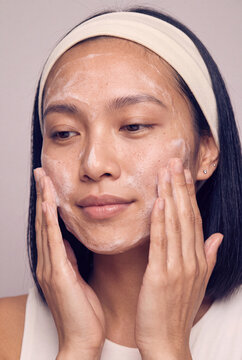Woman cleansing her face with foaming cleanser wearing a headband for a skincare routine tutorial and beauty background with gentle neutral tones
