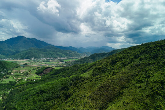 Massive gray clouds hover over the vibrant tropical slopes of the mountains in Hong Kong as daylight shifts across the landscape during the middle of the day