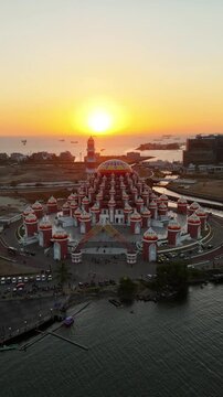Aerial view of Masjid Kubah 99 Asmaul Husna with its distinctive domes glowing during sunset by the waterfront in Kecamatan Mariso, Sulawesi Selatan, Indonesia.