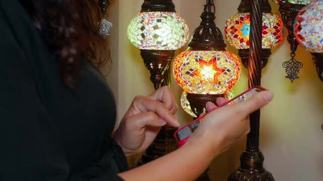 Customer inspects ornate Turkish mosaic lamp with vibrant stained glass pattern, hand touching illuminated decorative fixture in retail setting.