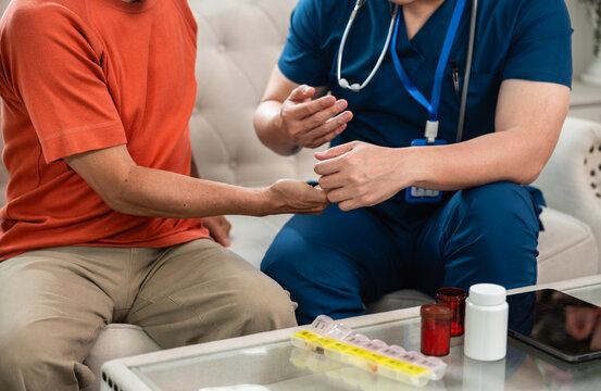 Senior Medication Management with a Male Nurse Guiding an Asian Elderly Man while Medicine Bottles, Pill Organizer and Digital Tablet Rest on a Table