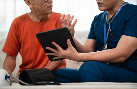 Senior Health Consultation with a Male Nurse Using a Digital Tablet beside an Asian Elderly Man and Blood Pressure Equipment during a Home Checkup
