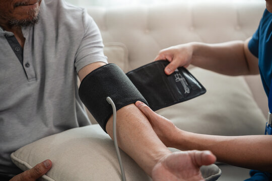 Senior Healthcare Professional Measuring Blood Pressure for an Asian Elderly Man with an Arm Cuff during a Home Health Checkup in a Close-Up View