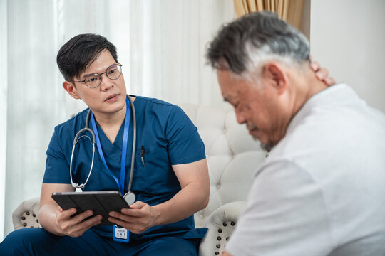 Male Nurse Consulting an Asian Senior Man with a Digital Tablet and Stethoscope during a Home Healthcare Visit in a Bright Living Room Interior