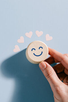 A top down view shows a hand holding a round, light colored wooden block printed with a simple blue smiling face emoji.