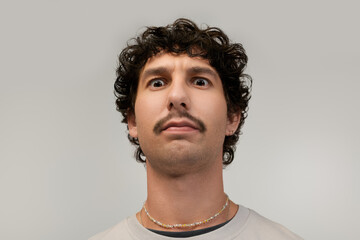 Obraz premium Young man with a distinctive moustache shows a playful expression in a light setting