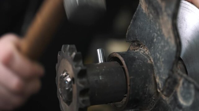 An engineer hammers a steel pin into a sprocket to tighten the chain for a snowmobile's drivetrain.