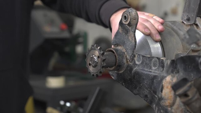 An engineer hammers a steel pin into a sprocket to tighten the chain for a snowmobile's drivetrain.