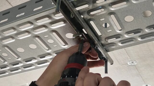 Slow motion close up of an electric impact driver fastening a lighting support clip onto a perforated cable tray.