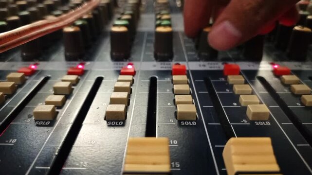 Close up of a sound engineer hand turning a knob on an analog audio mixer console in a recording studio