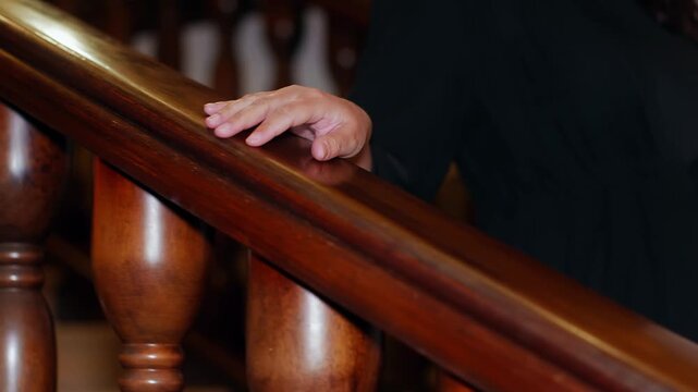 Young child places hand on polished wooden banister rail, suggesting safety, guidance, movement through residential space with warm architectural details.