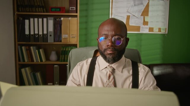 African American man wearing glasses, working at retro computer in vintage office. Footage suits nostalgic corporate training or historical technology documentaries