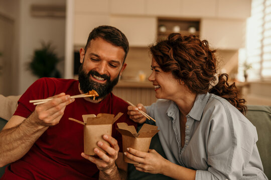 Happy couple enjoying takeout food with chopsticks at home