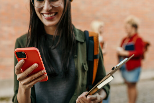 Young student smiling and using smartphone on campus