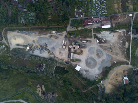 Aerial view of a sand mining and gravel processing site with piles of aggregate, heavy machinery, and surrounding agricultural fields in Kecamatan Tempel, Daerah Istimewa Yogya, Indonesia.