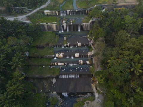 Aerial view of Grojogan Watu Purbo featuring stepped waterfalls and stone dams surrounded by lush tropical vegetation in Kecamatan Tempel, Daerah Istimewa Yogya, Indonesia.