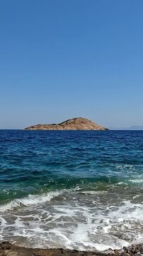 Vertical zoom out footage of a small rocky islet in the Greek sea. Clear blue sky at the background.