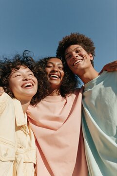 Group of smiling friends with arms around under blue sky for youth community poster and outdoor lifestyle background