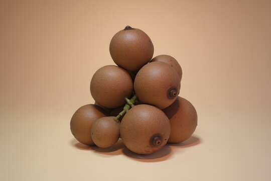 Stack of brown tropical fruits arranged in a small pyramid on a plain beige background with soft shadow.