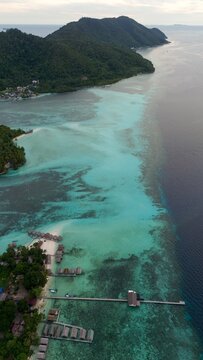 Aerial view of the turquoise waters and coral reefs surrounding the wooden overwater bungalows of a resort in the Raja Ampat Islands, Waigeo Barat, Southwest Papua, Indonesia.