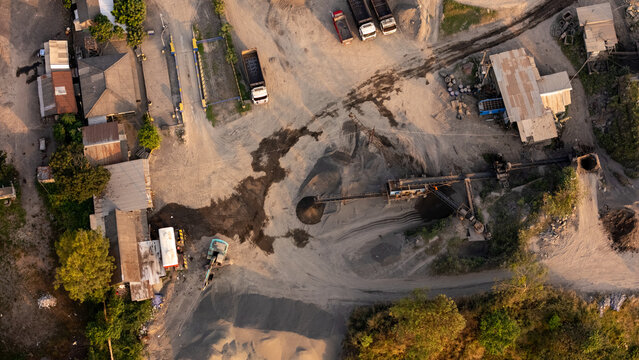 Aerial view of a sand and gravel mining site with heavy machinery, trucks, and piles of aggregate in an industrial area in Klaten, Central Java, Indonesia.